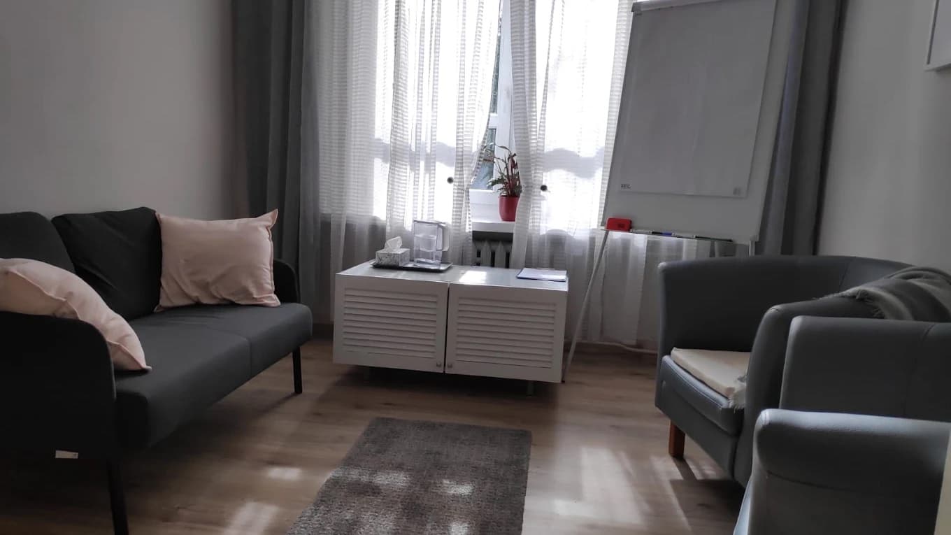 Gabinet: kanapa z poduszkami, fotele i flipchart przy oknie